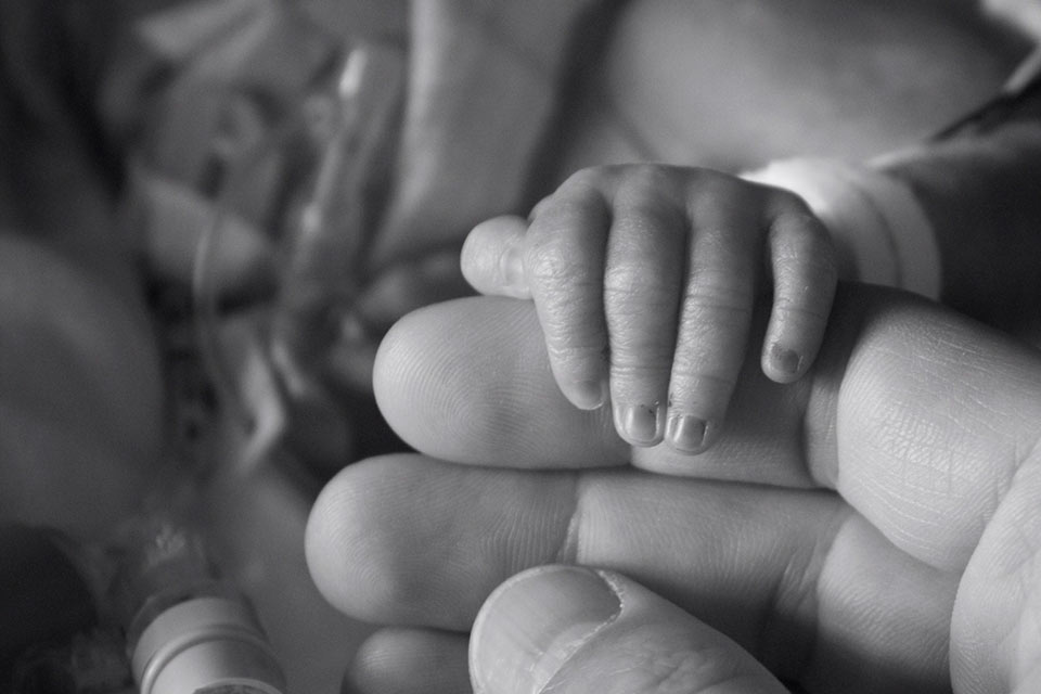 A prematurely born little baby holds his little hand around one of dad's fingers. 