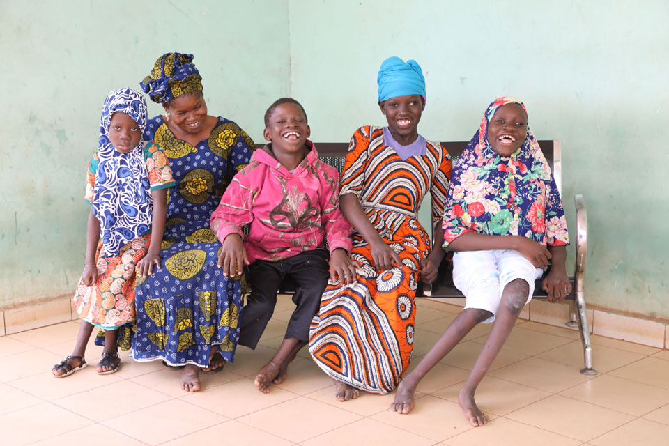 A woman sits with four children on a bench. The woman looks at the children with a loving smile.