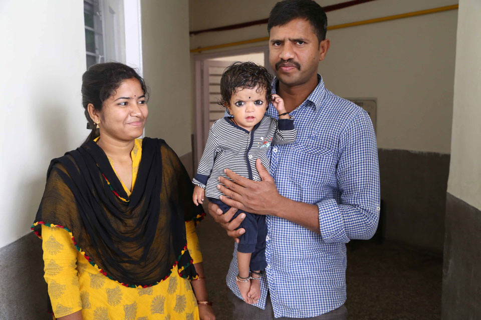 A little girl is carried by her father and her mother is standing next to her. The girl and her mother have a throwing mark on her forehead.